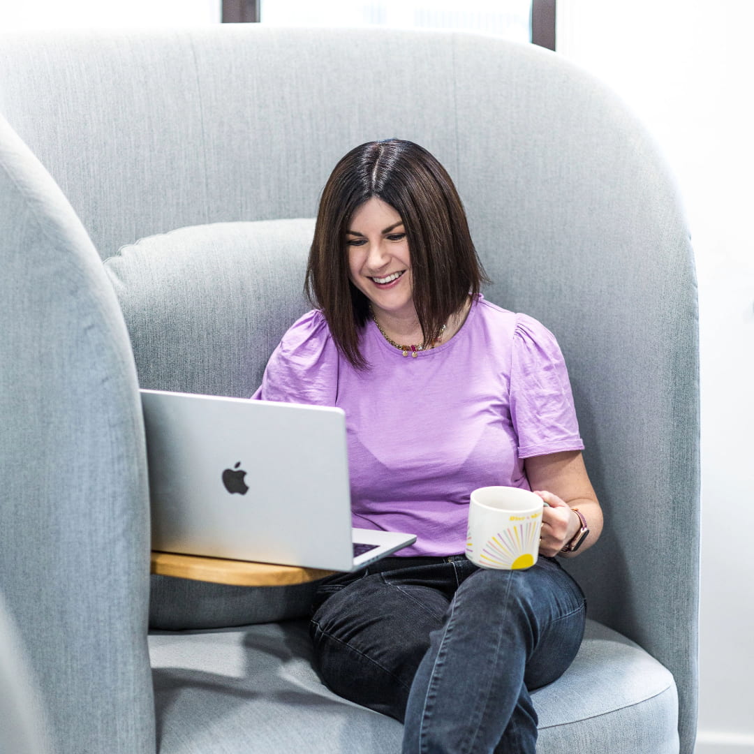 Rosie sitting in an armchair looking at her computer, smiling with a cup of coffee